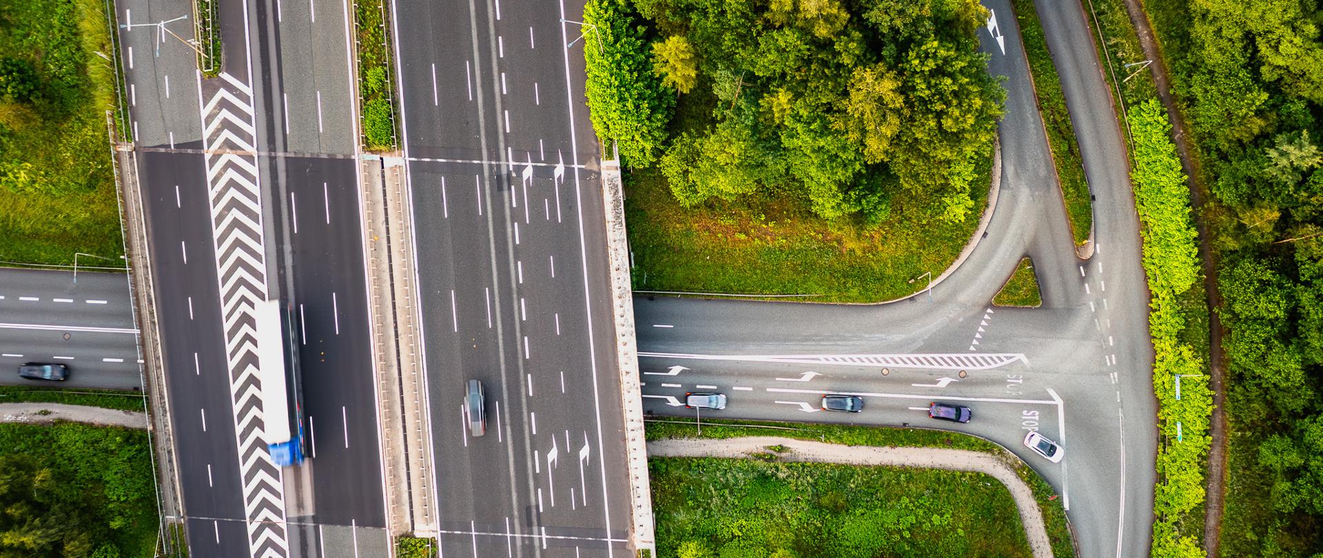 Trójpasmowa autostrada z dwoma pasami włączenia (lewa strona fotografii) i wyłączenia (po prawej stronie) w pobliżu węzła drogowego na przecięciu z lokalnym układem drogowym.