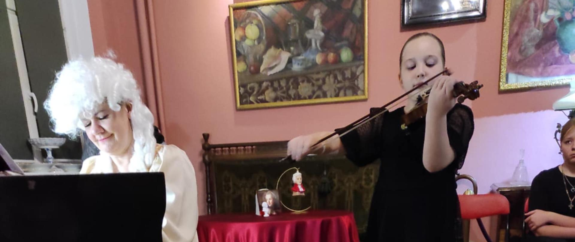 Uczennica grająca na skrzypcach, nauczycielka w stylowej peruce grająca na fortepianie.