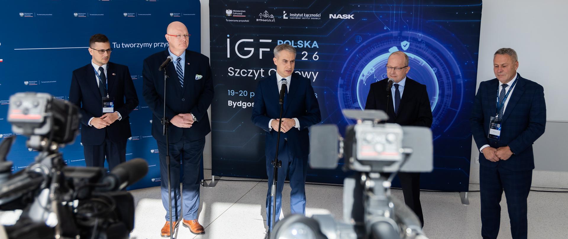 5 mężczyzn na tle ścianki przed kamerami 