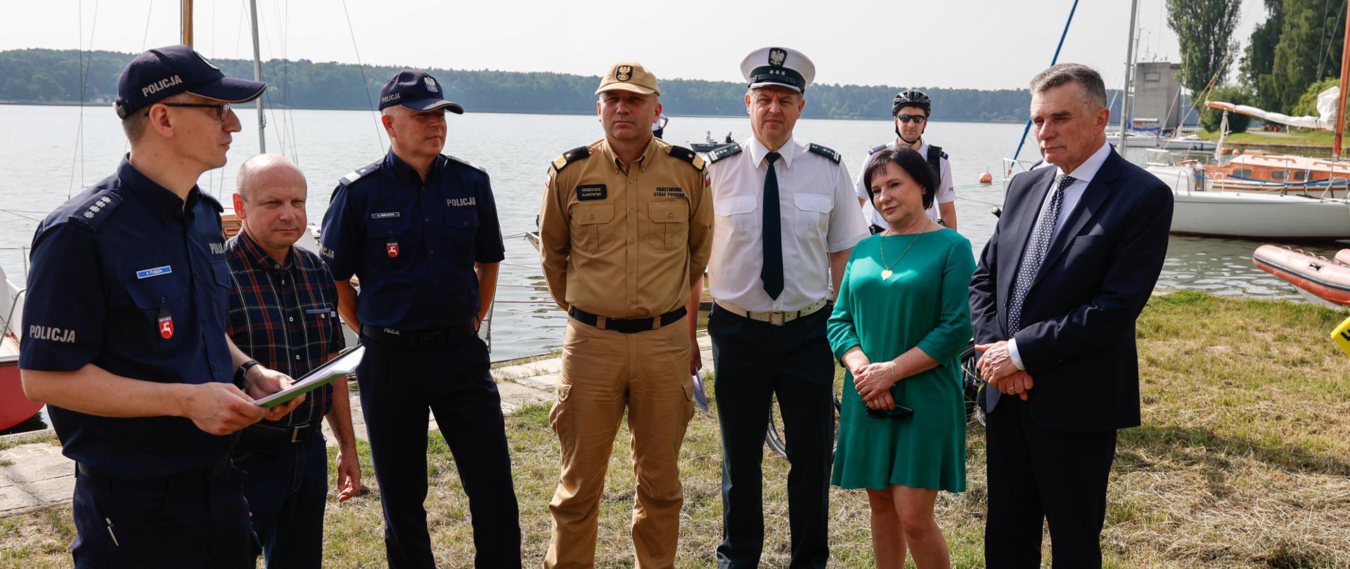 Mężczyźni i kobiety na konferencji prasowej. W tle zbiornik wodny.