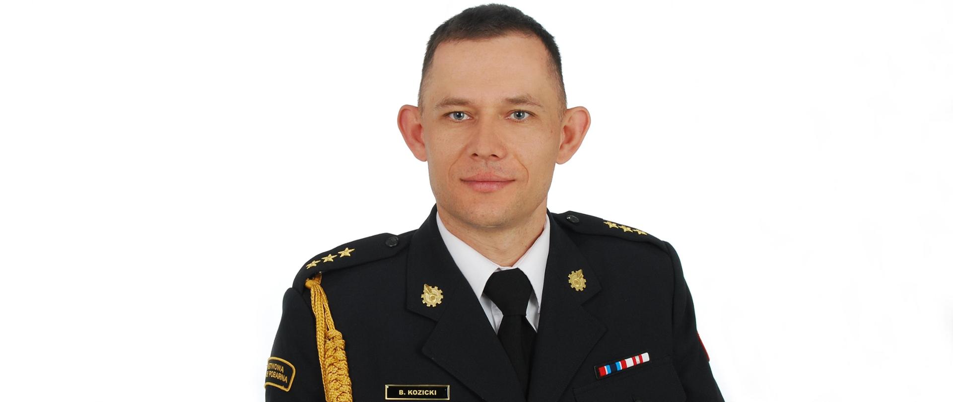 Zdjęcie przedstawia uśmiechniętego w średnim wieku mężczyznę na białym tle w mundurze galowym. 