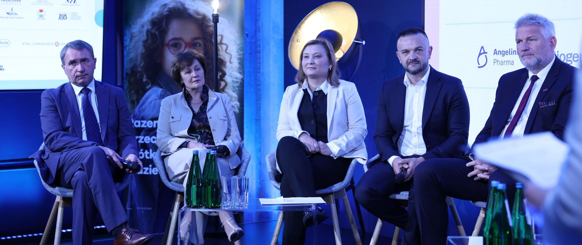 Wiceminister siedzi na krześle na scenie otoczona osobami i bierze udział w panelu dyskusyjnym. 