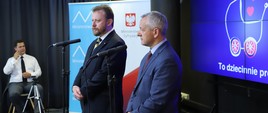 Minister zdrowia - Łukasz Szumowski i minister cyfryzacji - Marek Zagórski. W tle tłumacz Polskiego Języka Migowego.