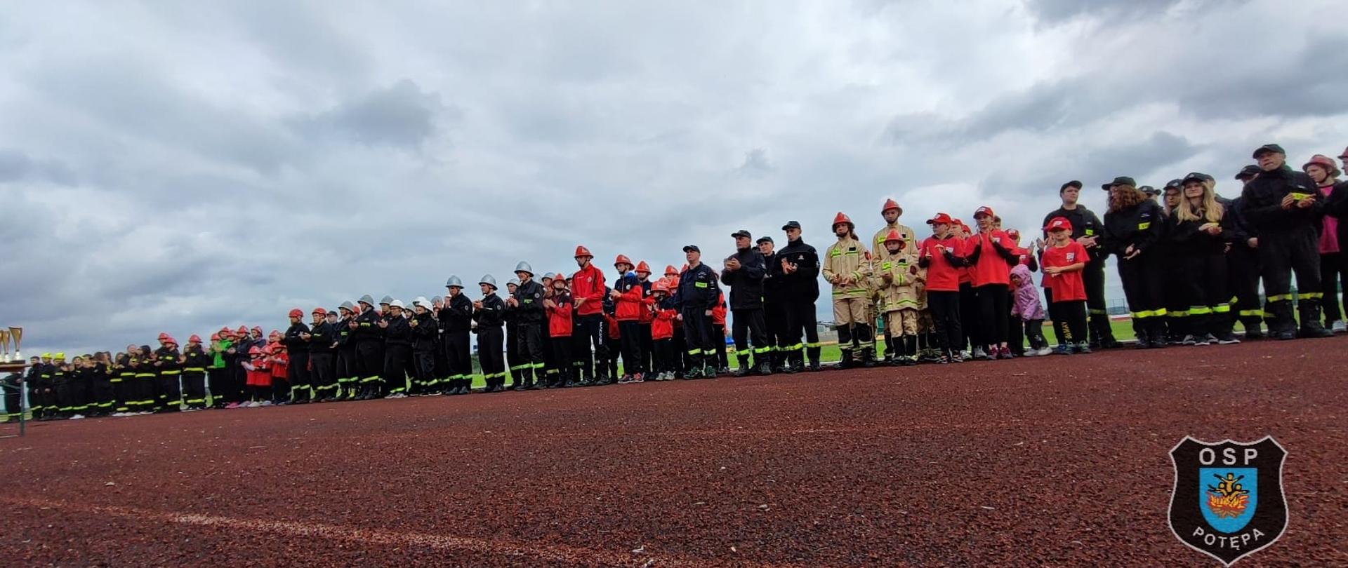 Strażacy w mundurach stoją w szeregu na boisku