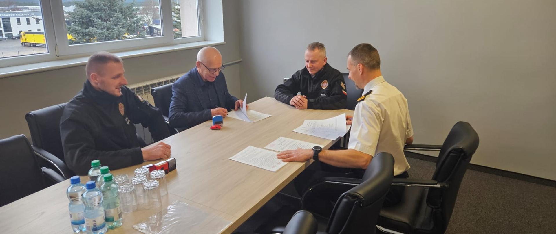 Trzech mężczyzn przy stole w czasie podpisywania dokumentów porozumienia.