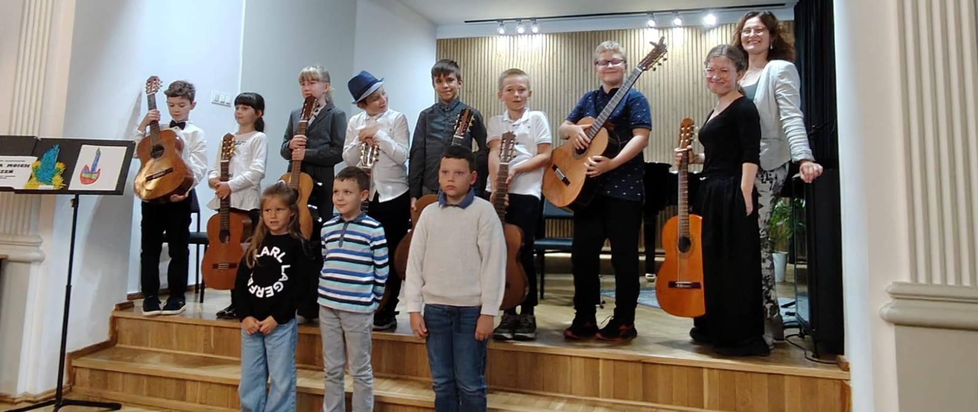 Galeria 9 zdjęć z koncertu klasy gitary p. A. Kozakowskiej pt. "Gitara wróciła z wakacji", który odbył się 23 września 2025 w auli PSM w Kłodzku. Uczniowie grają na gitarze w sali koncertowej.