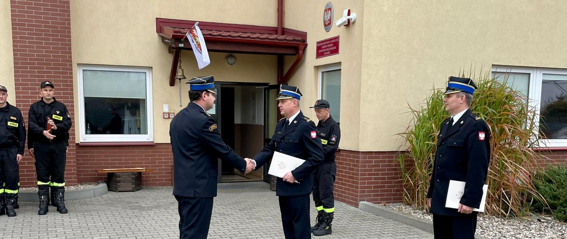 Komendant Miejski PSP wręcza akt mianowania dowódcy JRG 2. W tle budynek JRG 2.