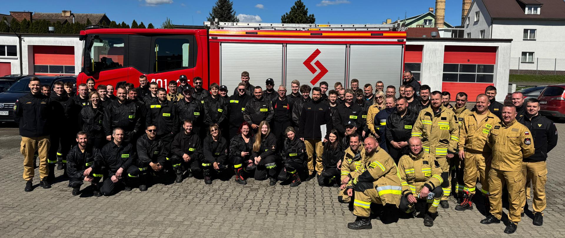Fotografia przedstawia zdjęcie grupowe wszystkich uczestników kursu podstawowego dla ochotniczych straży pożarnych. Fotografia wykonana na placu komendy.