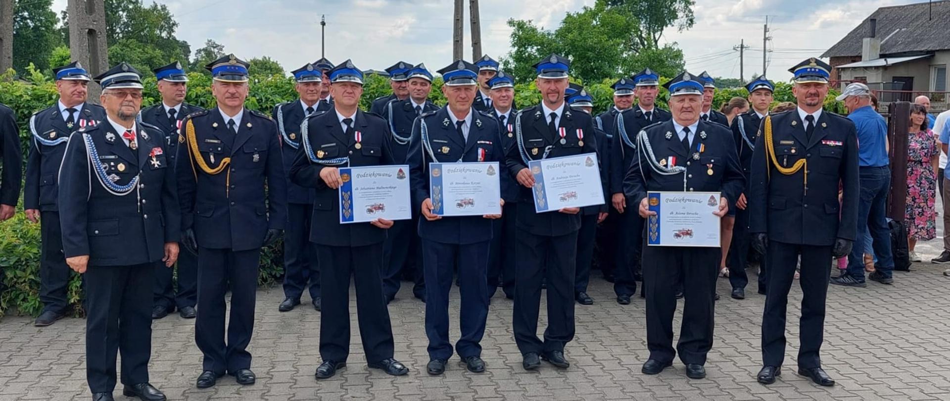 pięciu druhów osp i dwóch strażaków pozuje do zdjęcia czterech druhów prezentuje otrzymane dyplomy, z nimi stoją inni druhowie osp