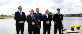 Konferencja, przemawia minister Marek Gróbarczyk. Obok stoją wojewoda zachodniopomorski Tomasz Hinc, posłowie Leszek Dobrzyński i Artur Szałabawki oraz dyrektora Urzędu Morskiego w Szczecinie Wojciech Zdanowicz. W tle zbiornik wodny, w oddali most.