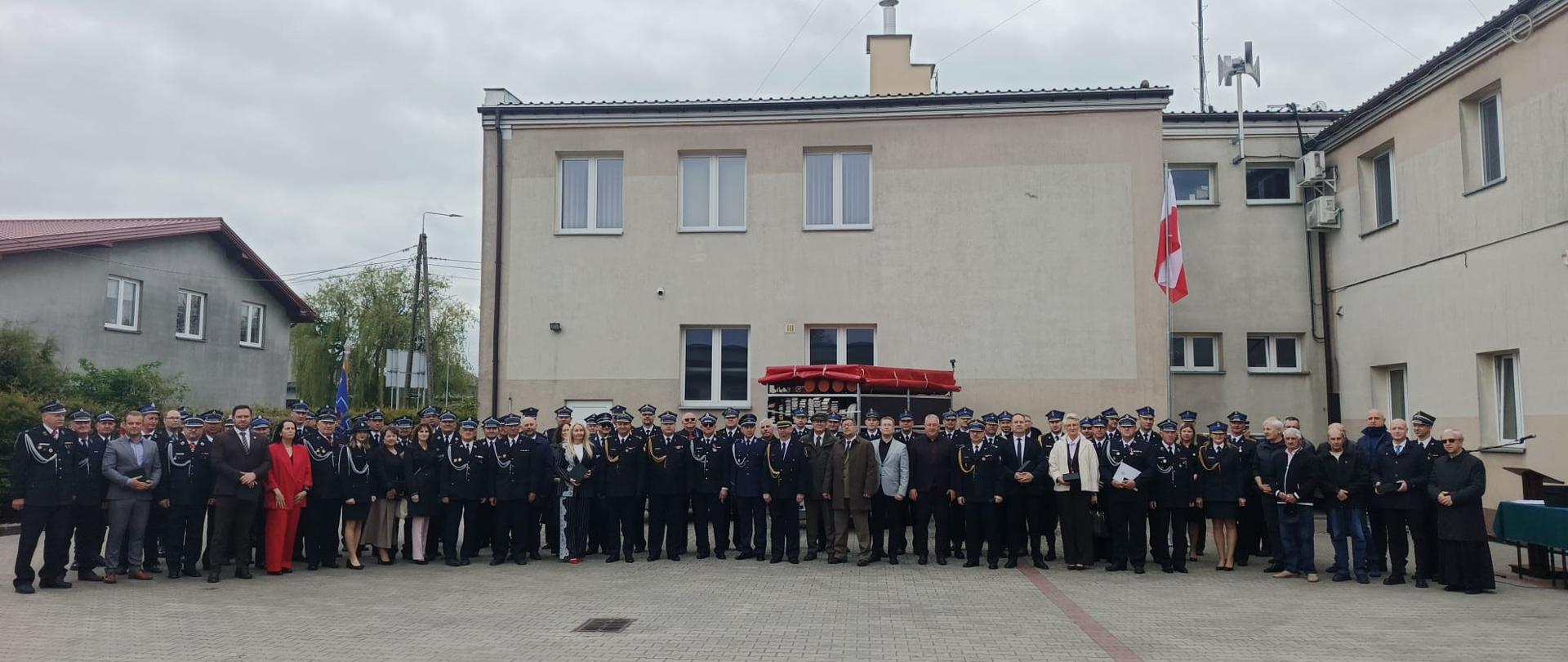 Na placu przed budynkiem jednostki zgromadziła się liczna grupa strażaków oraz zaproszonych gości, aby wspólnie zapozować do pamiątkowego zdjęcia. To zbiorowe portretowanie stanowi uroczyste podsumowanie obchodów, podkreślając jedność i profesjonalizm formacji w dniu ich święta.