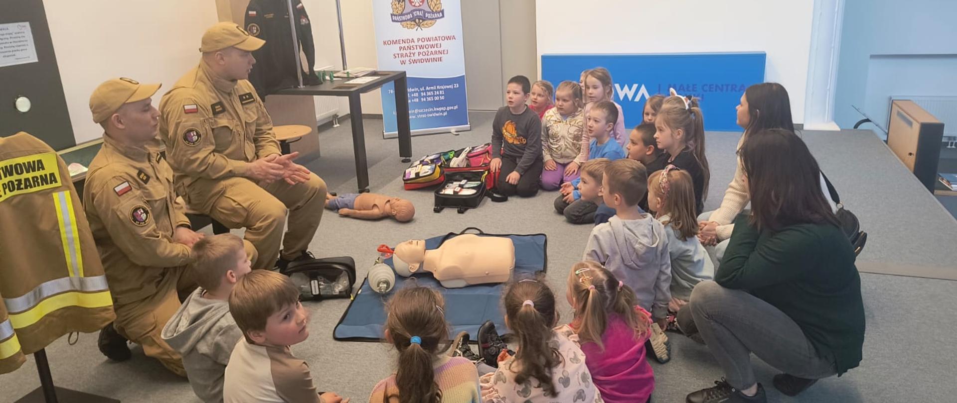 Zdjęcie przedstawia dzieci oraz strażaków podczas prelekcji w Centrum Nauki CORDIS w Świdwinie, strażacy udzielają instruktarzu pierwszej pomocy.