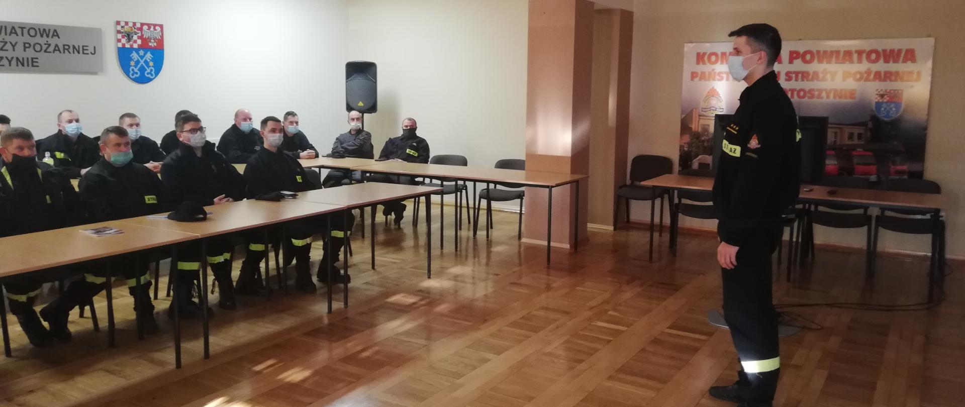 Zdjęcie przedstawia uczestników szkolenia oraz prowadzącego szkolenie. Byli to strażacy z jednostek OSP, siedzą przy stołach, mają założone maseczki chirurgiczne.