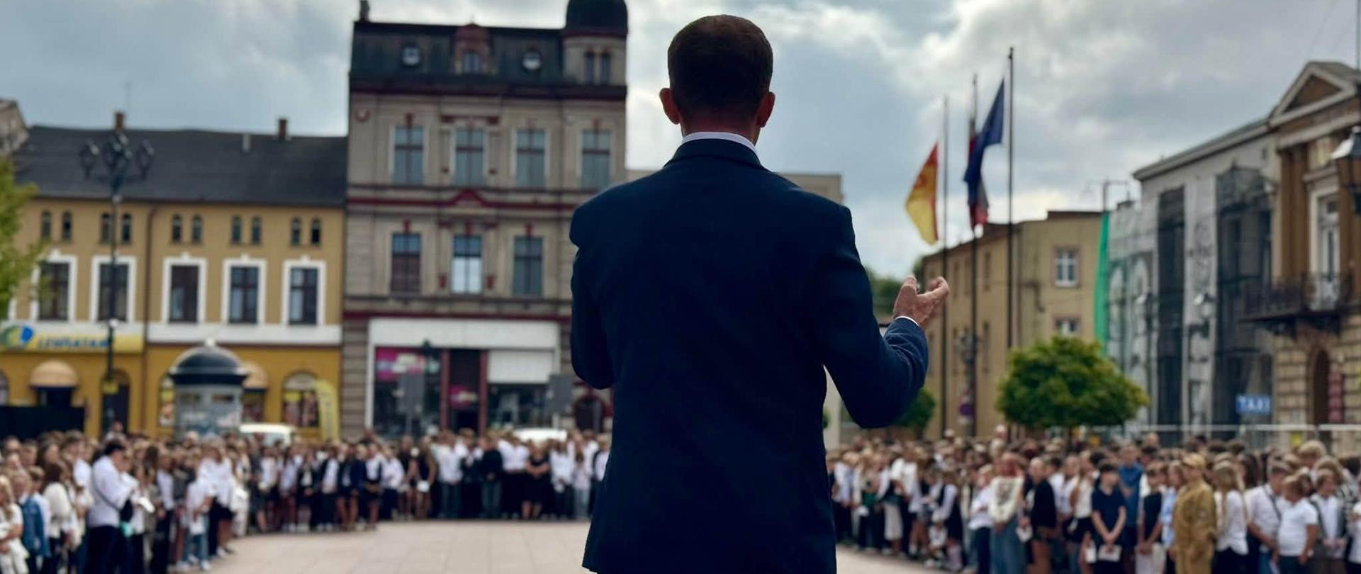 Mężczyzna stoi tyłem zwrócony ku grupy dzieci, 