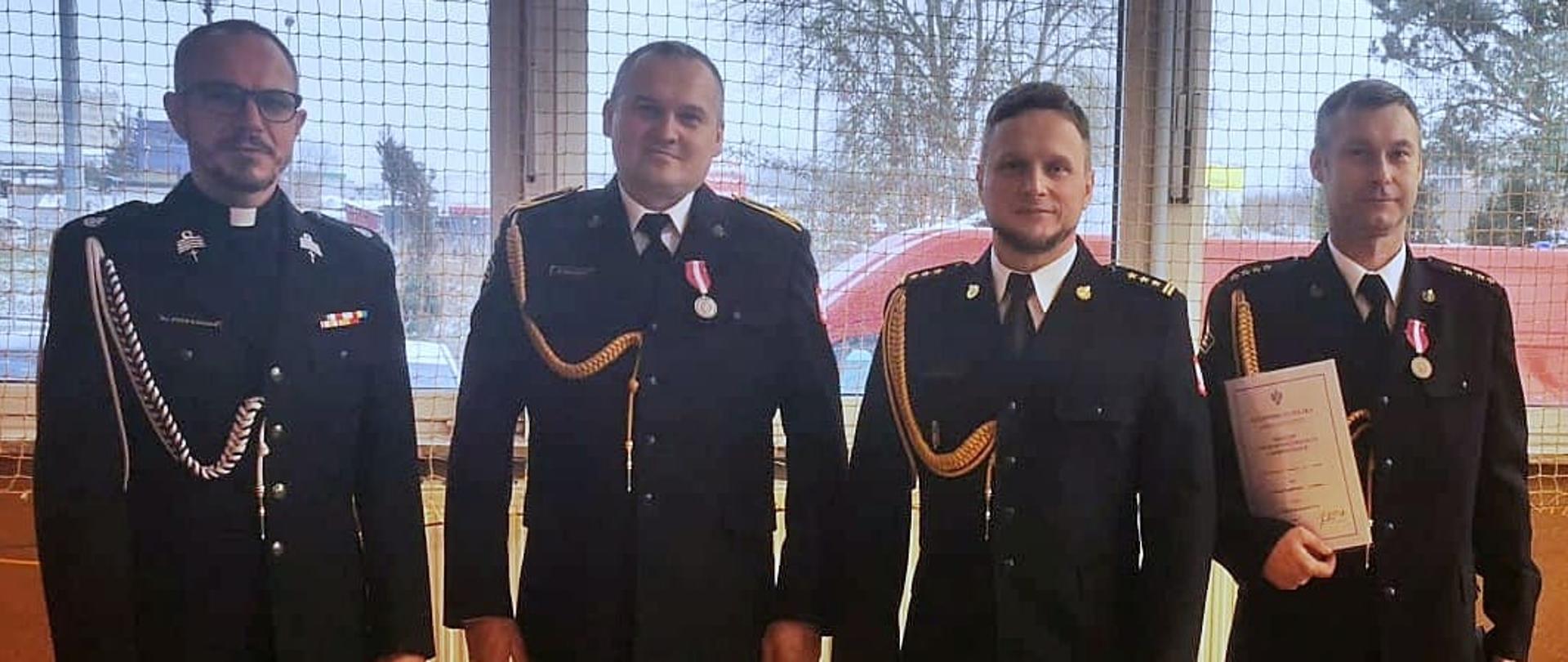 W pomieszczeniu stoi cztery osoby w ciemnych mundurach.