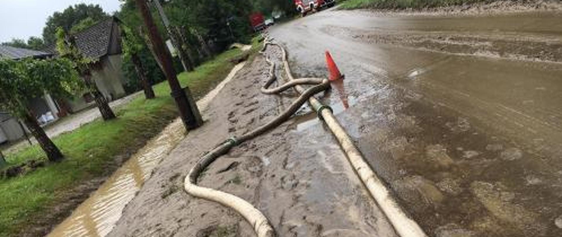 Droga po ustąpieniu opadów. Wcześniej zalana wodą. Widoczne naniesione błoto oraz rozwinięte linie wężowe w celu przepompowywania wody.
