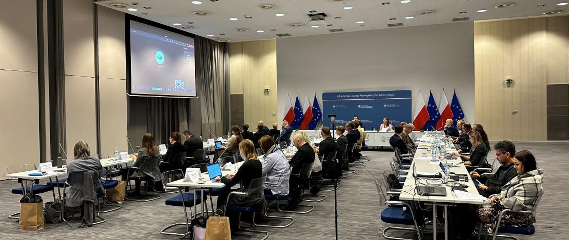 Na zdjęciu są przedstawieni siedzący w trzech rzędach przedstawiciele z Polski oraz z Komisji Europejskiej (także online) podczas posiedzenia Komitetu Monitorującego, który odbył się w dni 16.11.2023 w gmachu MSWiA 