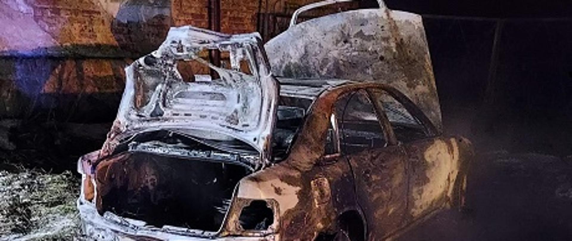 Zdjęcie przedstawia samochód osobowy marki Audi, który uległ całkowitemu spaleniu.