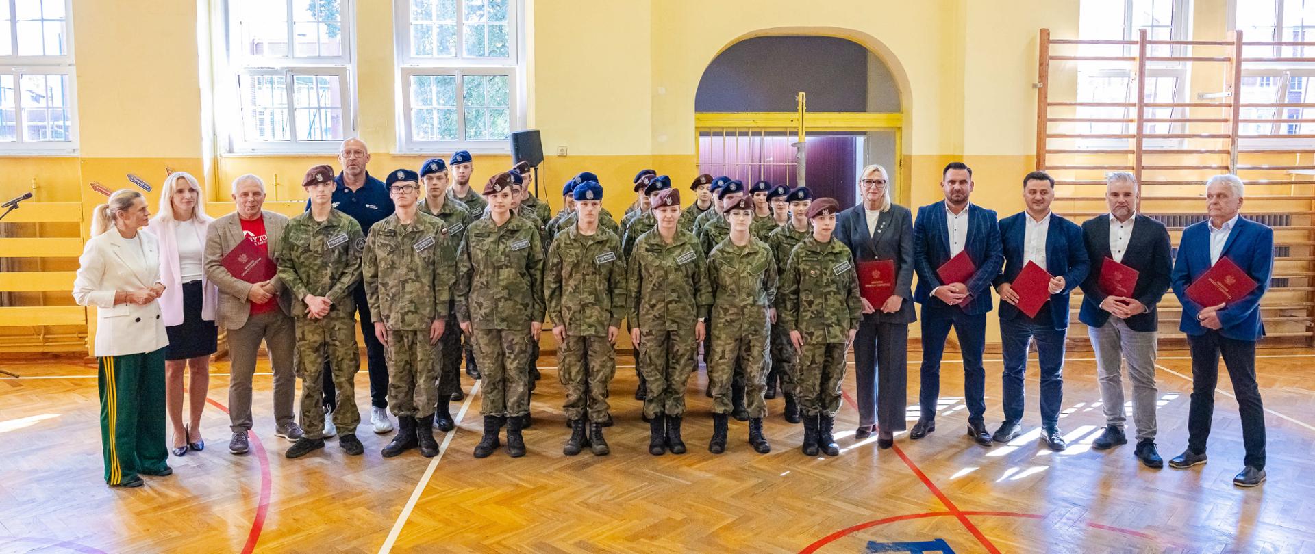Zdjęcie zbiorowe uczestników konferencji prasowej w Bytowie. Wśród nich minister sportu i turystyki Jakub Rutnicki oraz ministra edukacji Barbara Nowacka. Zdjęcie zrobione na sali gimnastycznej.