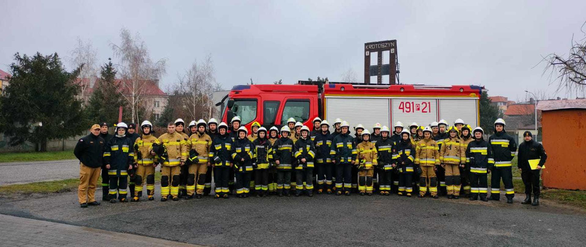 Zdjęcie ukazuje strażaków - ochotników na tle pojazdu pożarniczego na placu komendy powiatowej w Krotoszynie. Druhowie w ubraniach specjalnych po zakończeniu szkolenia.