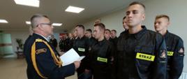 NNa zdjęciu młodzi strażacy odbierają z rąk Kujawsko-Pomorskiego Komendanta Wojewódzkiego PSP nadbrygadiera Jacka Kaczmarka teczki ze Ślubowaniem Strażaka