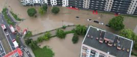 Widok na kamienice wykonane z drona. Z wysokości widać kamienicę, zalane chodniki, zalane samochody. Z boku z lewej strony widoczne pojazdy pożarnicze.