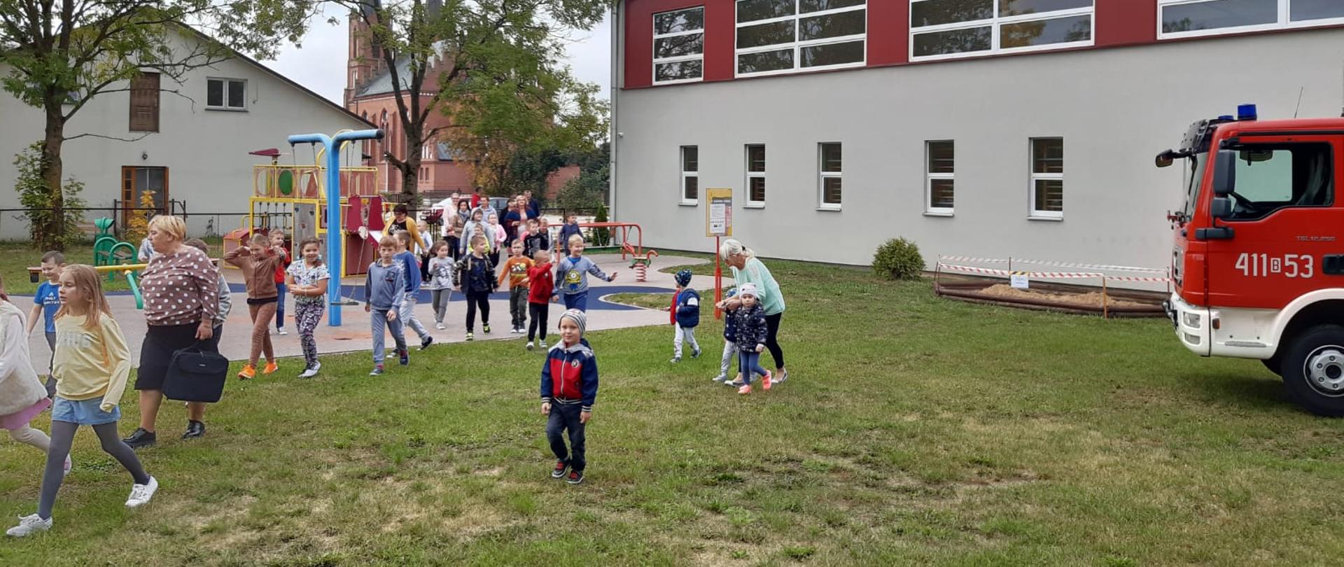 Zdjęcie przedstawia ewakuacje dzieci i nauczycieli z budynku 