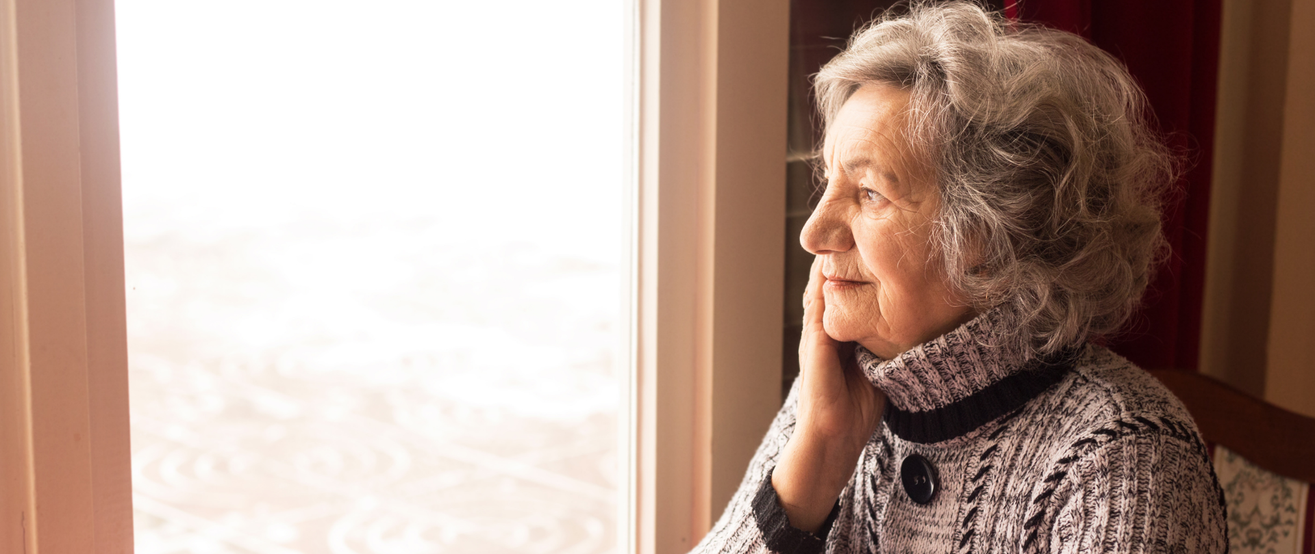 Kobieta w starszym wieku siedząca przy stole, spoglądająca w okno.