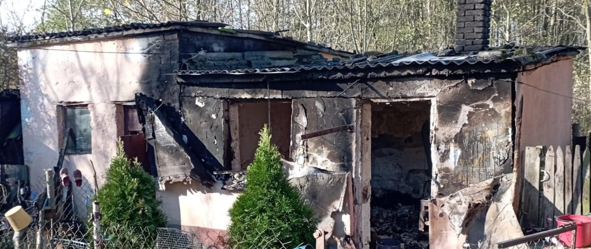 Zdjęcie przedstawia użytkowy budynek gospodarczy, w którym doszło do pożaru. Okno i drzwi się spaliły, widać okopcenia całego obiektu.