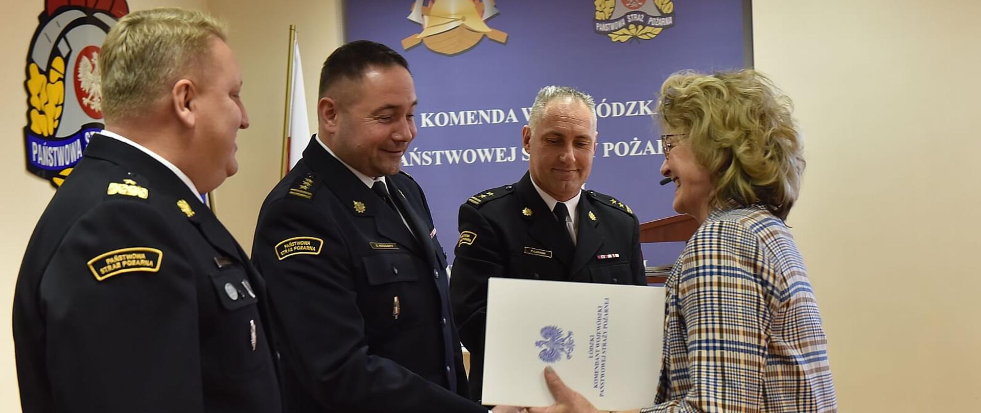 trzech strażaków w mundurach galowych gratuluje kobiecie w żakiecie, zdjęcie w sali konferencyjnej