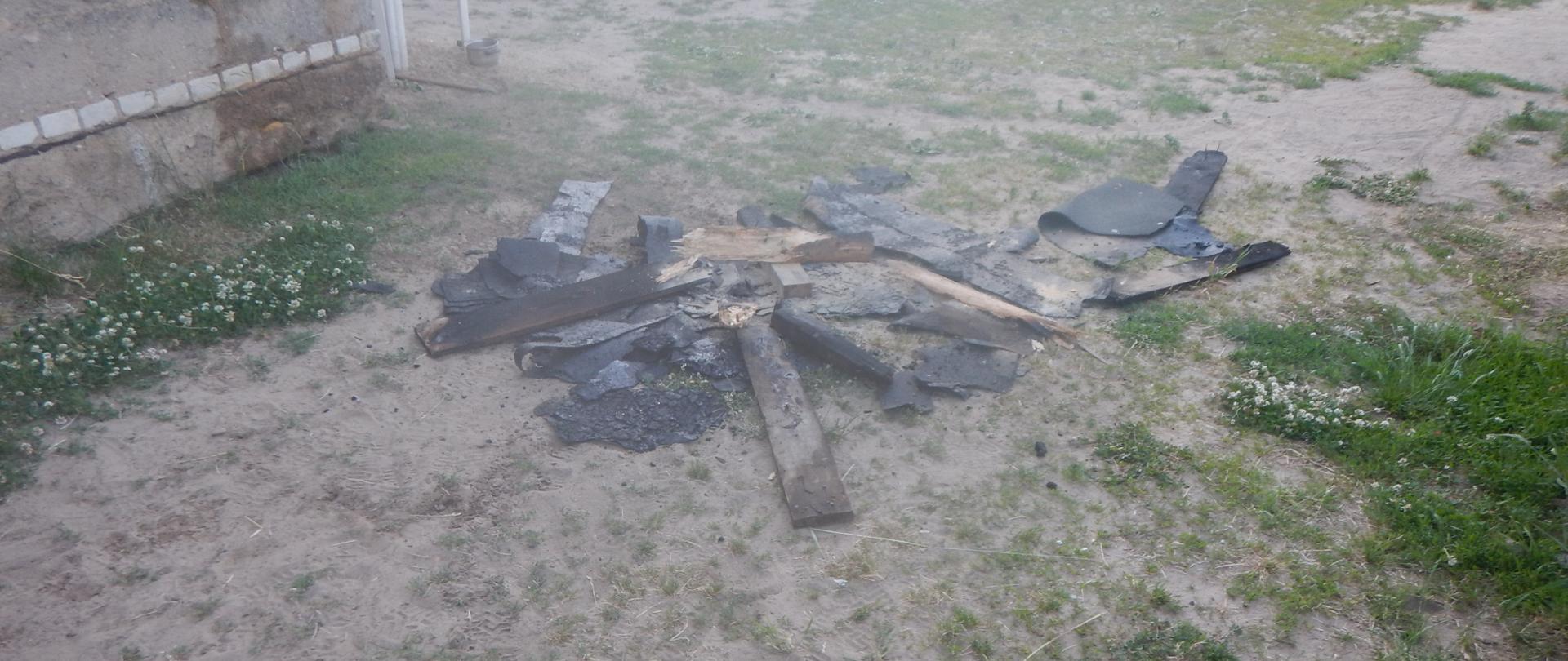 Zdjęcie przedstawia elementy poszycia dachowego, które uległy spaleniu. Deski znajdują się na podwórku posesji.