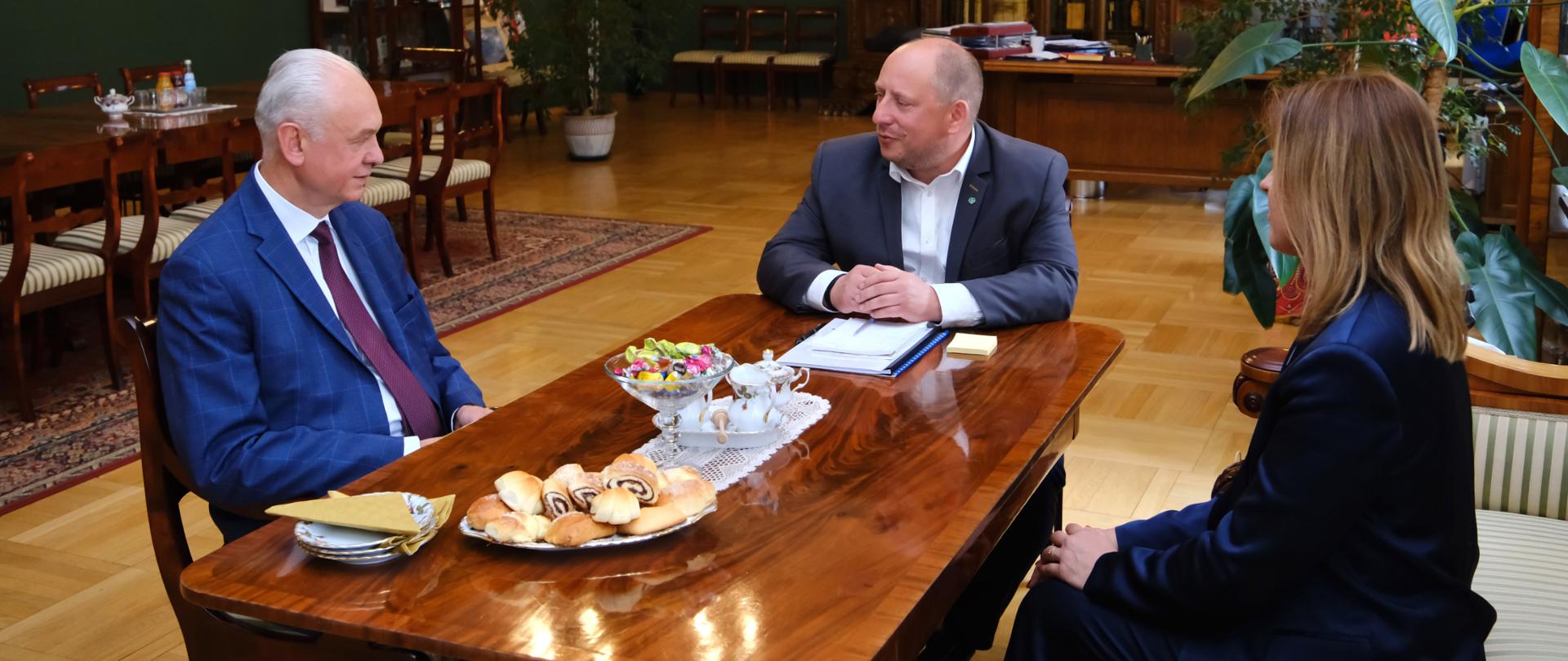 Trzy osoby (dwóch mężczyzn i jedna kobieta) siedzący przy stole