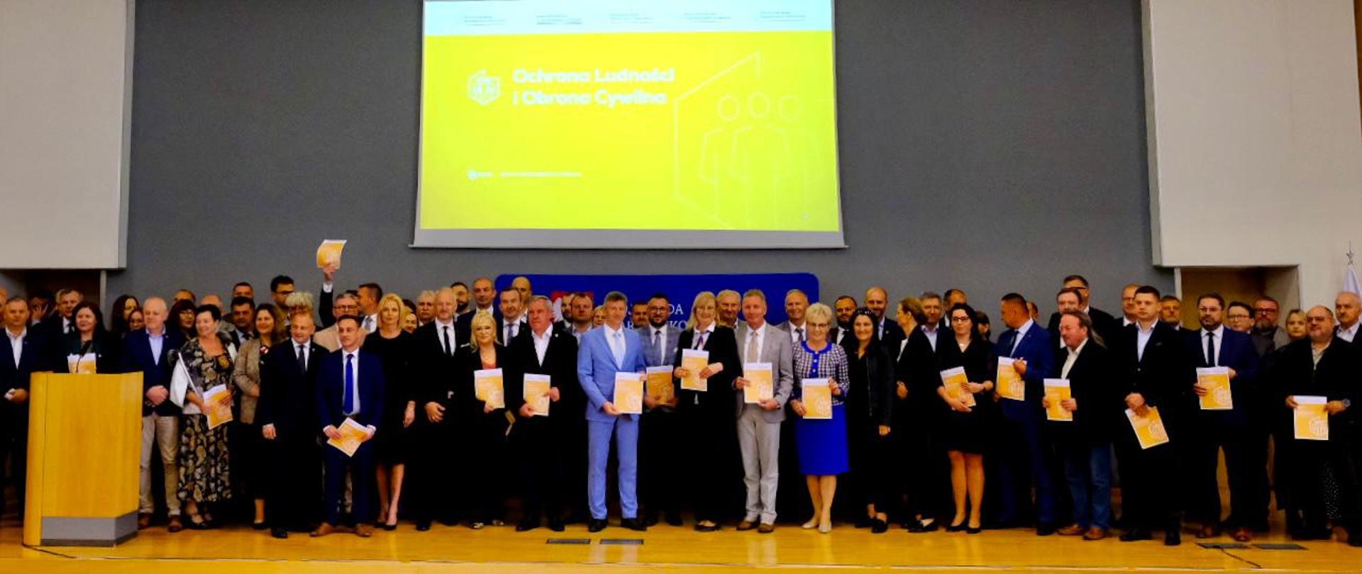 Kilkanaście osób stoi na scenie i pozuje do zdjęcia 