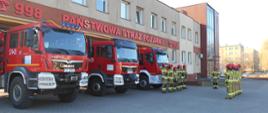 Zdjęcie przedstawia strażaków na zmianie służby przed budynkiem Komendy Powiatowej na tle samochodów pożarniczych oddających hołd poległy strażakom z Ukrainy 
