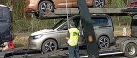Kontrola drogowa ciężarówki przewożącej fabrycznie nowe samochody. Inspektor ITD ubrany w odblaskową kamizelkę stoi obok przyczepy i mierzy wysokość pojazdu z ładunkiem.