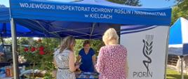 Dwie kobiety stojące tyłem do zdjęcia, trzecia kobieta stojąca pośrodku zdjęcia skierowana przodem do zdjęcia. Osoby znajdują się pod namiotem WIORiN.
