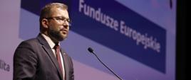 Minister funduszy i polityki regionalnej Grzegorz Puda na konferencji poświęconej Funduszom Europejskim dla kultury, minister stoi przy mównicy i przemawia do mikrofonu