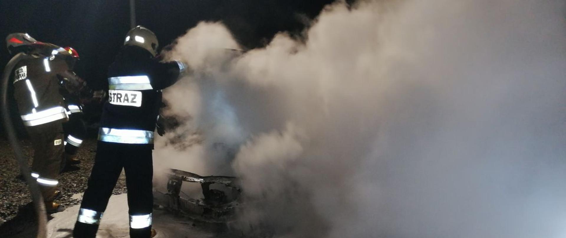 Dwóch strażaków podaje podaje pianę. na kłęby dymu. 