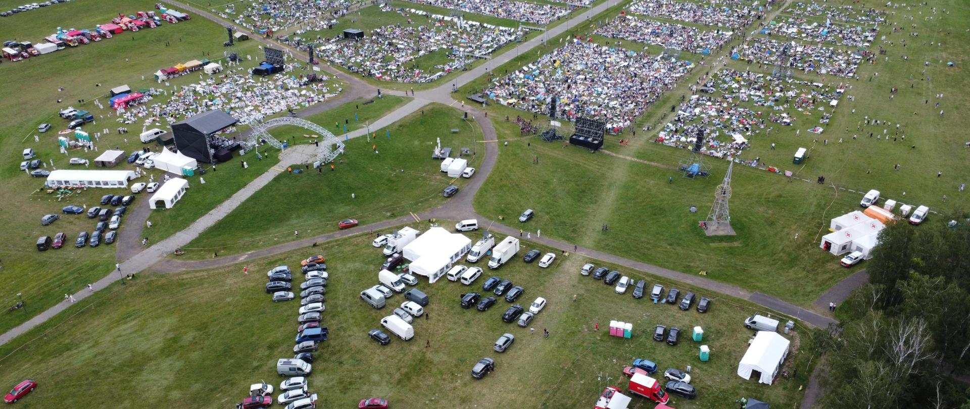 Widok na Pola Lednickie. Pojazdy, ołtarz, ludzie stoją na trawie.