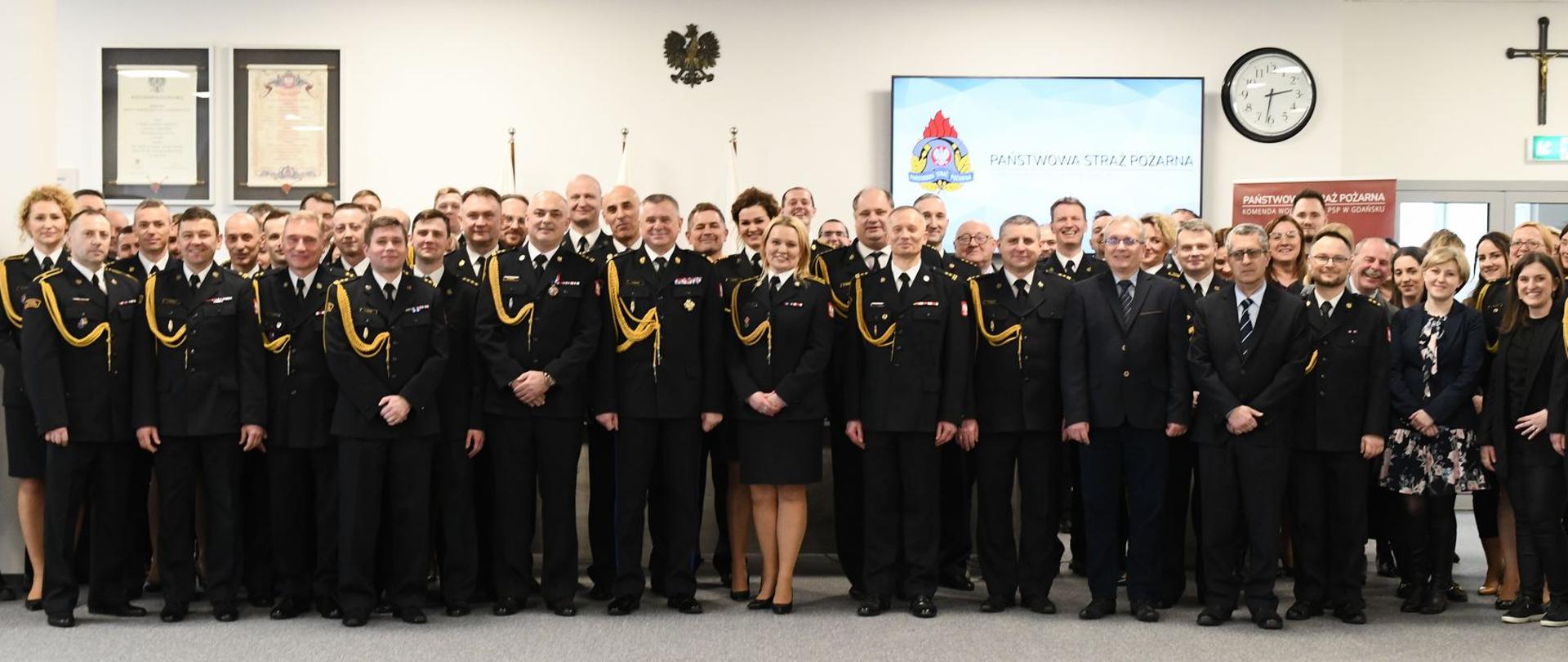 Strażacy oraz osoby cywilne stoją obok siebie.