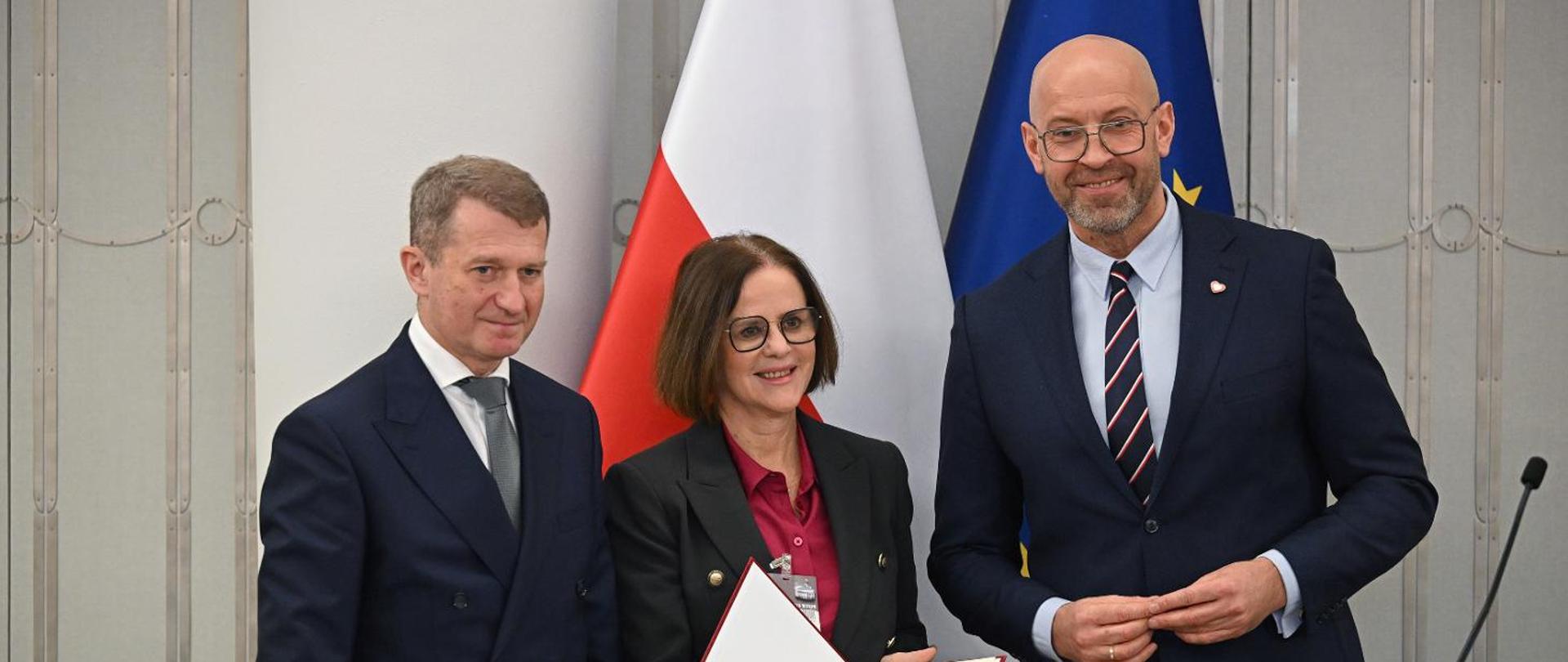 Picture. From left to right: Secretary of State in the Ministry of Sport and Tourism Ireneusz Raś, newly-appointed president of the Polish Tourism Organisation Magdalena Krucz, Minister of Sport and Tourism Jakub Rutnicki. Flagsof Poland and the EU in the background.