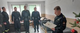 Zdjęcie wykonano w budynku Komendy Powiatowej Państwowej Straży Pożarnej w Sępólnie Krajeńskim w pomieszczeniu świetlicy. Strażacy Państwowej Straży Pożarnej w ubraniach koszarowych stoją w szeregu a Komendant Państwowej Straży Pożarnej starszy brygadier Maciej Suchomski odczytuje decyzję o awansie jednego ze strażaków.