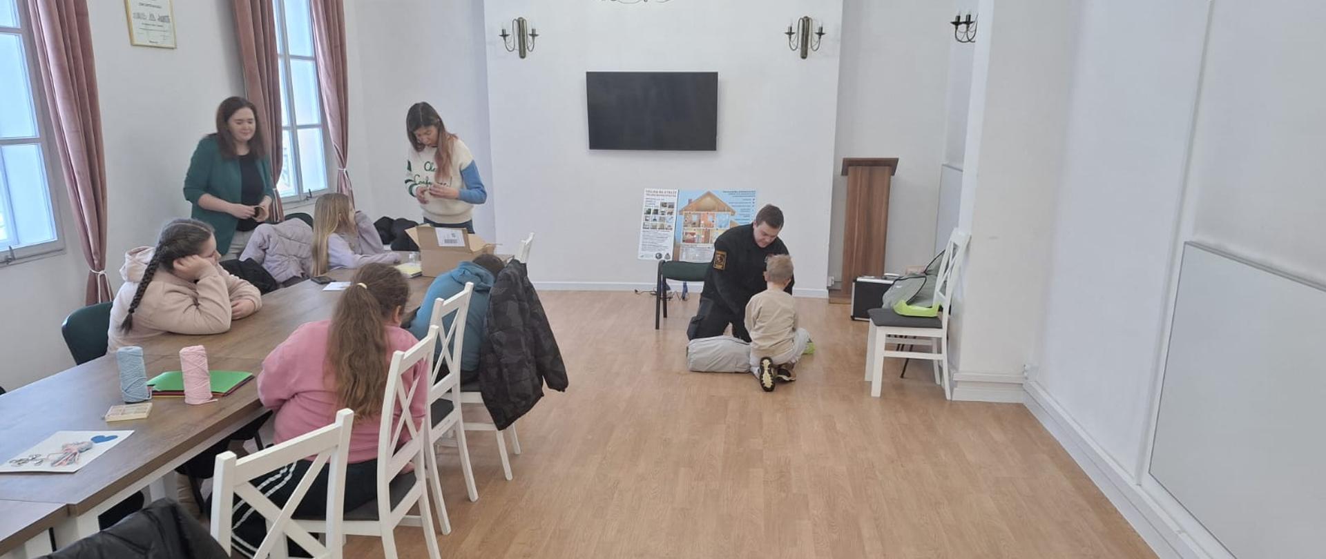 Strażak opowiada dzieciom o zagrożeniach związanych z spędzaniem ferii zimowych na świeżym powietrzu, a także o pierwszej pomocy. Uczestnicy wraz z opiekunami uważnie słuchają.