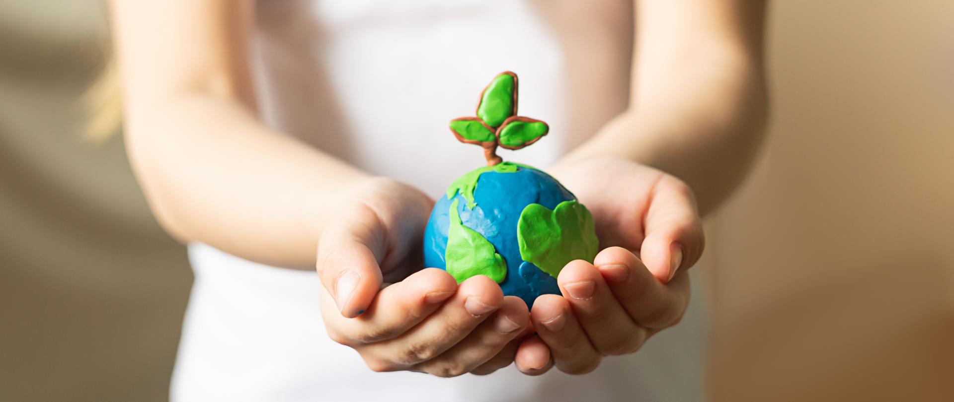 A small globe with trees in the hands of a child. Layout of the planet made of plasticine in children's palms. Concept ecology. Copy space. Horizontal frame.