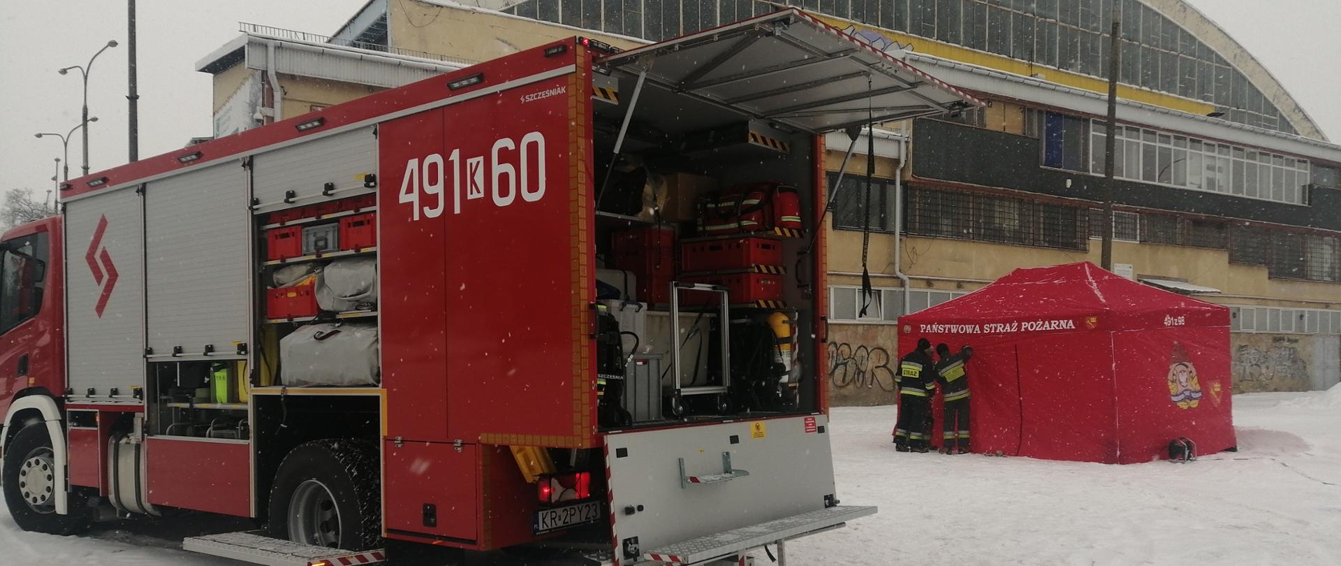 w tle Budynek Miejskiej Hali Lodowej, samochód średni ratownictwa chemicznego z JRG Nowy Targ, czerwony namiot do zabezpieczenia logistycznego działań, zdjęcie wykonane w warunkach zimowych, śnieg.