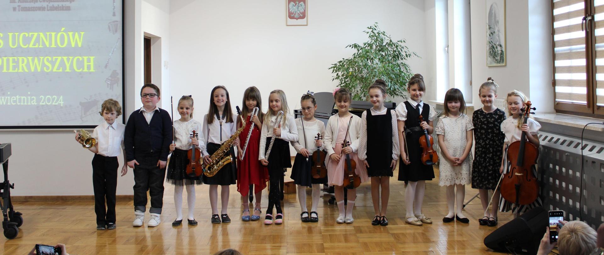 trzynastu uczniów na estradzie pozuje do zdjęcia z instrumentami po występie