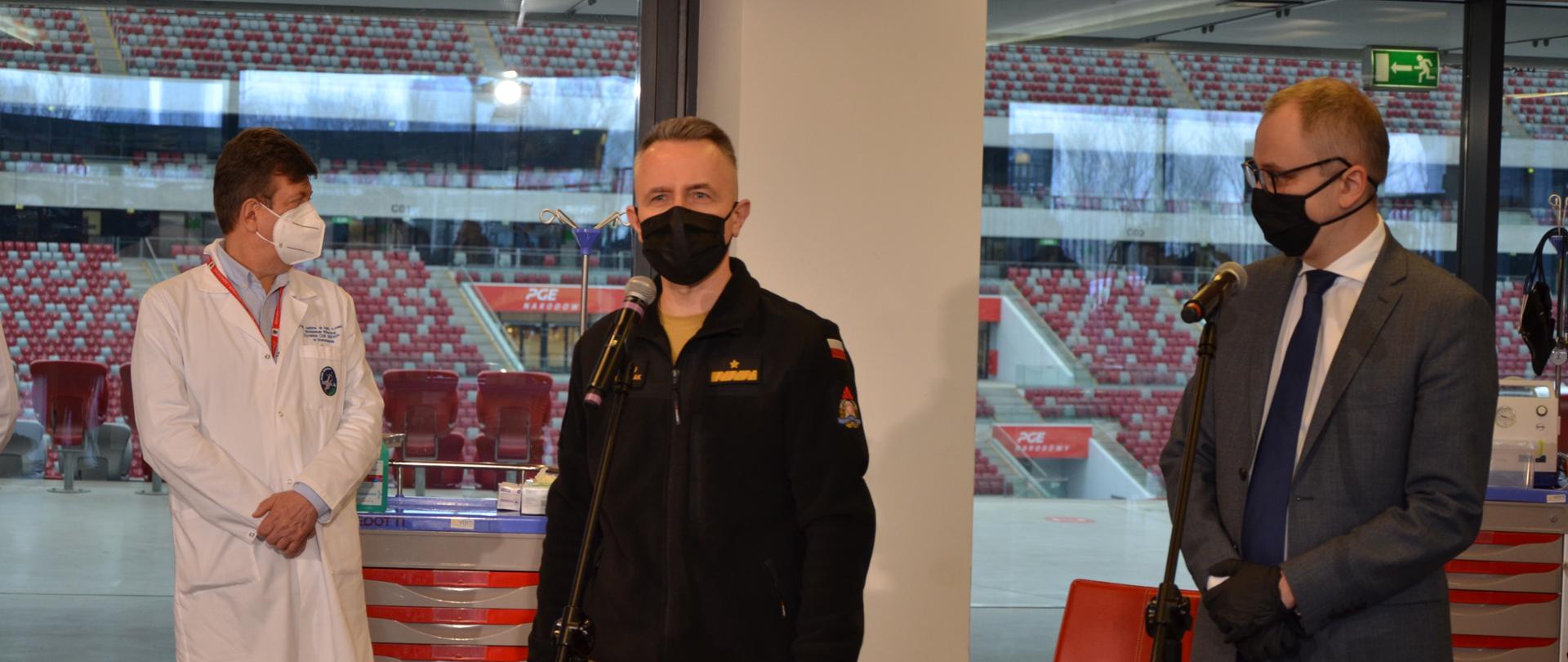 Briefing prasowy z udziałem wiceministra w MSWiA Pana Błażeja Pobożego a także komendantów głównych służb mundurowych podległych MSWiA w sprawie inauguracji procesu szczepień służb mundurowych. Przy mikrofonie przemawia nadbrygadier Andrzej Bartkowiak – komendant główny PSP,, obok stoi wiceminister Błażej Poboży, odpowiedzialny za służbę zdrowia MSWiA. W tle widoczny lekarz prof. nadzw. dr hab. n. med. Waldemar Wierzba Dyrektor Centralnego Szpitala Klinicznego MSWiA w Warszawie, który jako jeden z kilku lekarzy będzie realizował proces szczepienia komendantów głównych służb mundurowych podległych MSWiA w szpitalu tymczasowym na PGE Narodowym. 