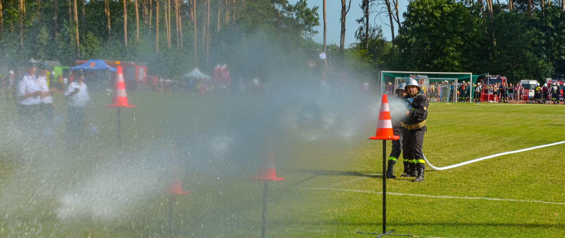 Strażacy strumieniem wody strącają pachołki