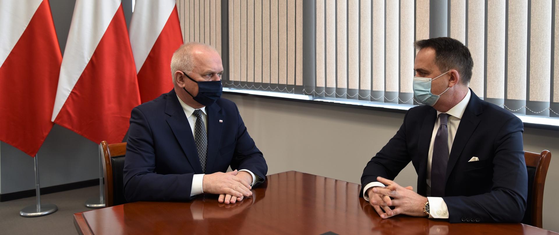 Wojewoda rozmawia z burmistrzem Łęknicy. Siedzą przy stole. W tle flagi