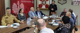 Zdjęcie przedstawia strażaków i samorządowców podczas spotkania dotyczącego Systemu ostrzegania i alarmowania.
W tle pomieszczenie.
